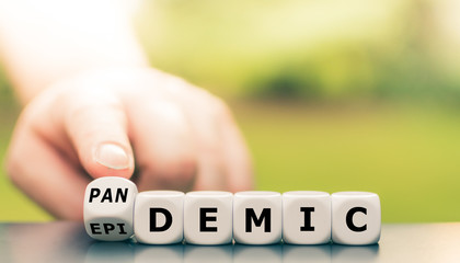 Hand turns a dice and changes the word epidemic to pandemic.