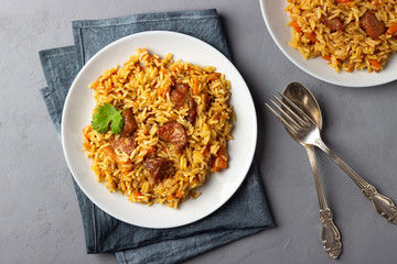 Traditional asian dish - pilaf from from rice, vegetables and meat in a plate on gray background. Top view.