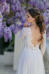 A bride in a wedding dress stands with her back to the camera under a tree.