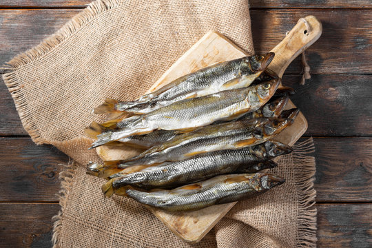 Smoked or dried smelt fish on a wooden Board on a brown wooden table. Top view with space for text	