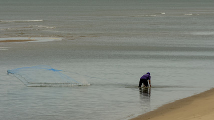 thai fisherman in the water with blue net at low tide