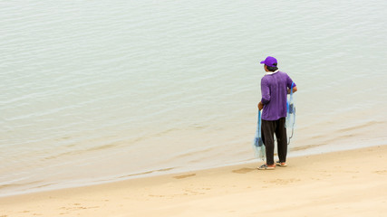 Thai fisherman at the water's edge with blue net at low tide