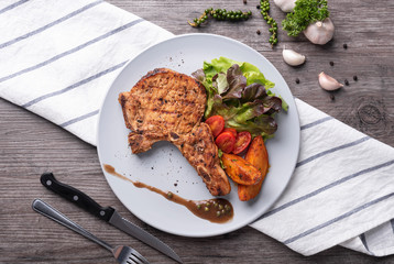 pork chop steak with vegetable salad and potato chips in white plate. top view.