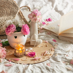 Candle and Vase with roses and peonies flowers and spring decor on the books