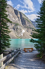 Turquoise waters of beautiful Moraine lake. Snow-covered Rocky mountains in summer day. log bench on the lake. Banff National Park