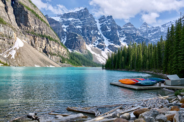 Turquoise waters of beautiful Moraine lake. Snow-covered Rocky mountains in summer day. Canoes on a...