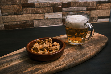 Torreznos and a beer jar on a wooden table. Spanish typical food, fried pork bacon. Appetizer.