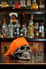 Human skull on a bar counter. Red skull in orange bandana on the background of bottles with...