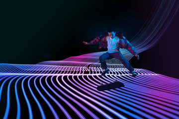 Caucasian young skateboarder riding on dark neon lighted line background. Training in action and...