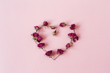 Heart symbol made of dry rose flower buds on pink background. Flatlay, top view Valentine's Day...