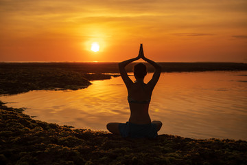 Yoga pose. Woman sitting on the beach, practicing yoga. Young woman raising arms with namaste mudra...