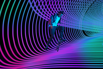 Caucasian young skateboarder riding on dark neon lighted line background. Training in action and motion on colorful waves. Concept of hobby, healthy lifestyle, youth, action, movement, modern style.