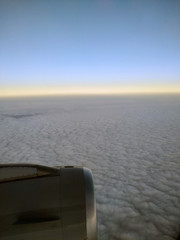 A jet engine is seen through the plane's window while flying over clouds at dawn