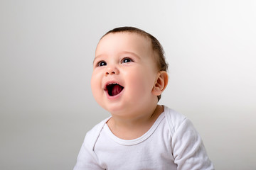 portrait of a baby boy looking at the camera in a white bodysuit on a white background, space for...