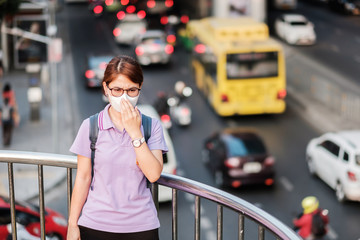 young Asian woman wearing N95 respiratory mask protect and filter pm2.5 (particulate matter) against traffic and dust city. healthcare and air pollution concept