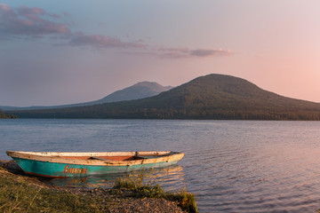 Fototapeta premium boat at the shore on the lake in the mountains at purple sunset with sun shining and reflecting in the water
