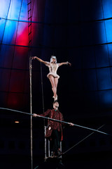 handsome gymnast supporting attractive acrobat while holding pole