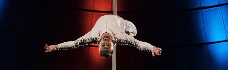 panoramic shot of strong acrobat with outstretched hands performing on metallic pole