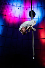 strong acrobat with closed eyes performing on metallic pole