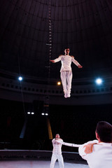 acrobats holding pole while handsome man jumping in circus