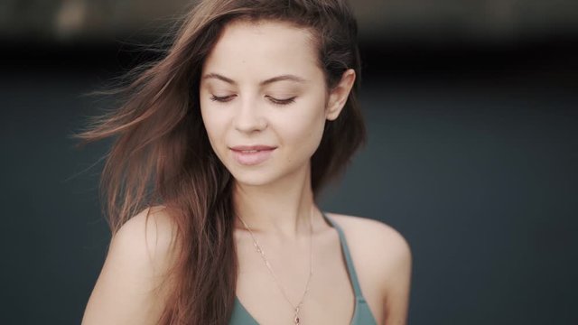 Portrait of beautiful young woman runs her hand through hair, looks at camera