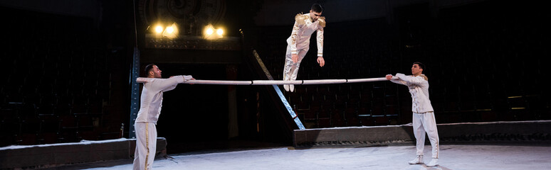 panoramic shot of gymnast exercising on pole near acrobats in circus