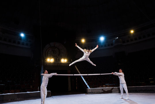 gymnast with outstretched hands jumping on pole near acrobats in circus