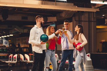 Group of friends toast with a beer in a bowling alley - obrazy, fototapety, plakaty