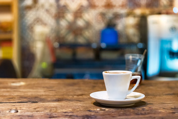 A white coffee espresso cup with plate on a wooden table, indoors.