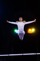 Fototapeta na wymiar handsome gymnast with outstretched hands jumping near pole in arena of circus