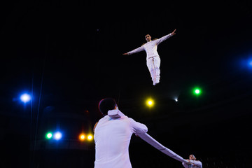 low angle view of air acrobat with outstretched hands jumping near pole in arena of circus