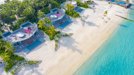 Maldives coastline, aerial landscape of luxury villas with white sand and palm trees. Paradise island aerial view, amazing blue sea and luxury vacation background