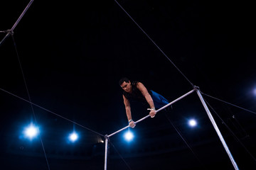 Fototapeta na wymiar low angle view of handsome acrobat performing on horizontal bars in circus