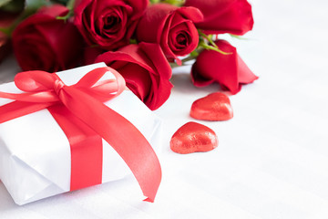 Red rose bouquet and white gift with red ribbon bow. Giving present concept.Copy space