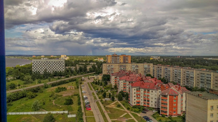 View from the balcony of the city with a bend in the river and low Cumulus clouds with breaking rays of the sun and a band of rain on the horizon