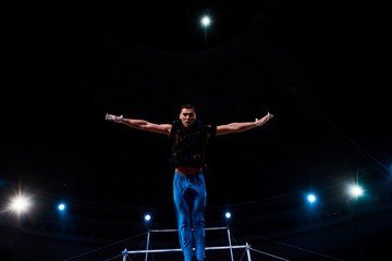 Fototapeta na wymiar athletic gymnast with outstretched hands performing near horizontal bars in arena of circus