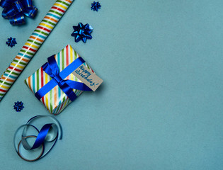 The concept of birthday. Gift box in beautiful packaging, gift wrapping paper, bows and ribbon on a blue-gray background. Free space.