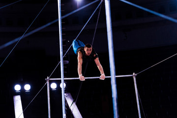 selective focus of athletic gymnast performing on horizontal bars in arena of circus