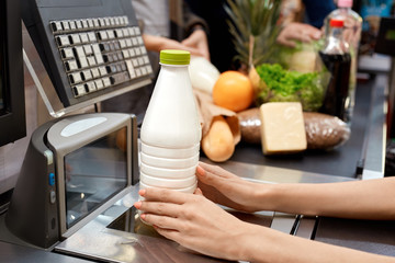 Daily Shopping. People standing in queue at checkout counter while cashier checking out bottle of milk close-up