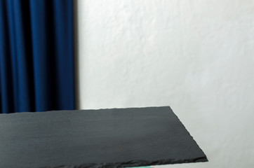Closeup of empty slate tray against white wall and dark blue drapes.Template for prducts, cafe, etc.
