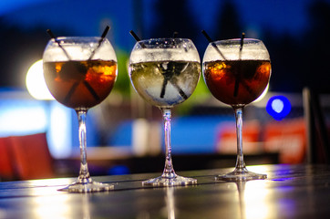 Beautiful row line of different colored alcohol cocktails on a party, martini, vodka,and others on decorated catering bouquet table on open air event, picture with beautiful bokeh