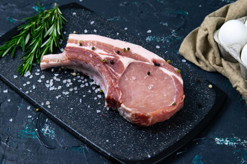 Raw t-bone steak stands on a marble board along with rosemary