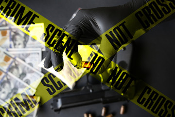 Gun lying on the table. Man in black gloves holding bullets. Illegal drug selling. Crime scene do...