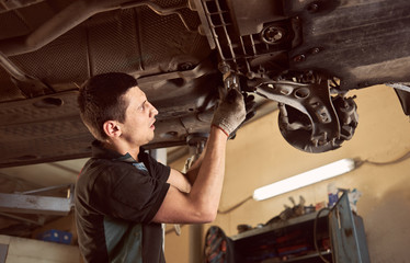 Repairman fixing car in garage. Experienced specialist car mechanic standing under lifted car...