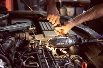 Car mechanic repairing diesel engine with screwdriver and flashlight helping in garage workshop. Close up view of old dirty auto engine and cropped car mechanic skilful hands. Car repairing concept