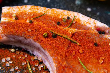 Raw pork steak on the bone sprinkled with red pepper near rosemary, corn, eggs and bell pepper.