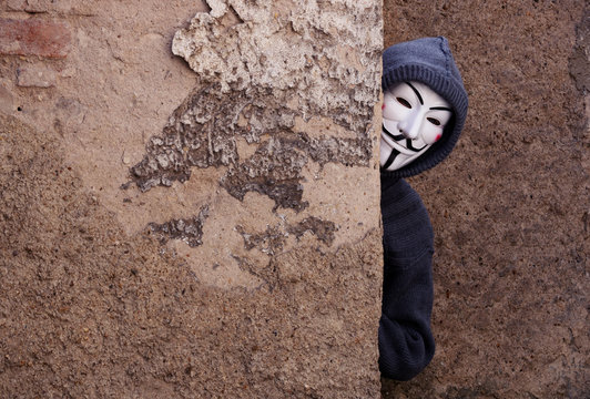 Velvary, CZECH REPUBLIC &ndash; February 27, 2019: An unidentified man is wearing the Vendetta mask and standing in front of a wall, the mask is a symbol of a hackers group Anonymous