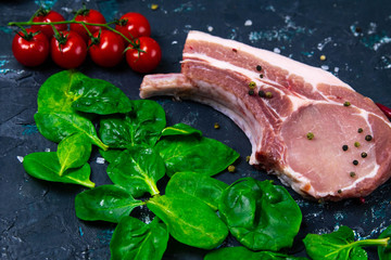 Raw pork steak on the bone sprinkled with red pepper near rosemary, corn, eggs and bell pepper