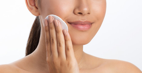 Girl applying lotion using cotton pad, white background