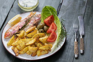 Grilled fish with roasted potatoes and vegetables on the plate, red mullet fish.